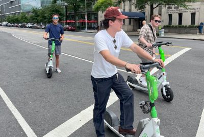 Students riding e-scooters pause on a city street. 