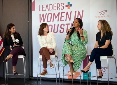 four women sitting on tall chairs in front of a Women in Industry-branded backdrop